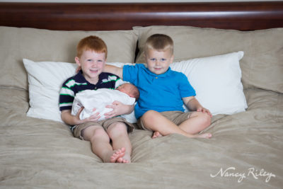 newborn with brothers on bed