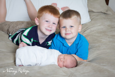 newborn with brothers on bed
